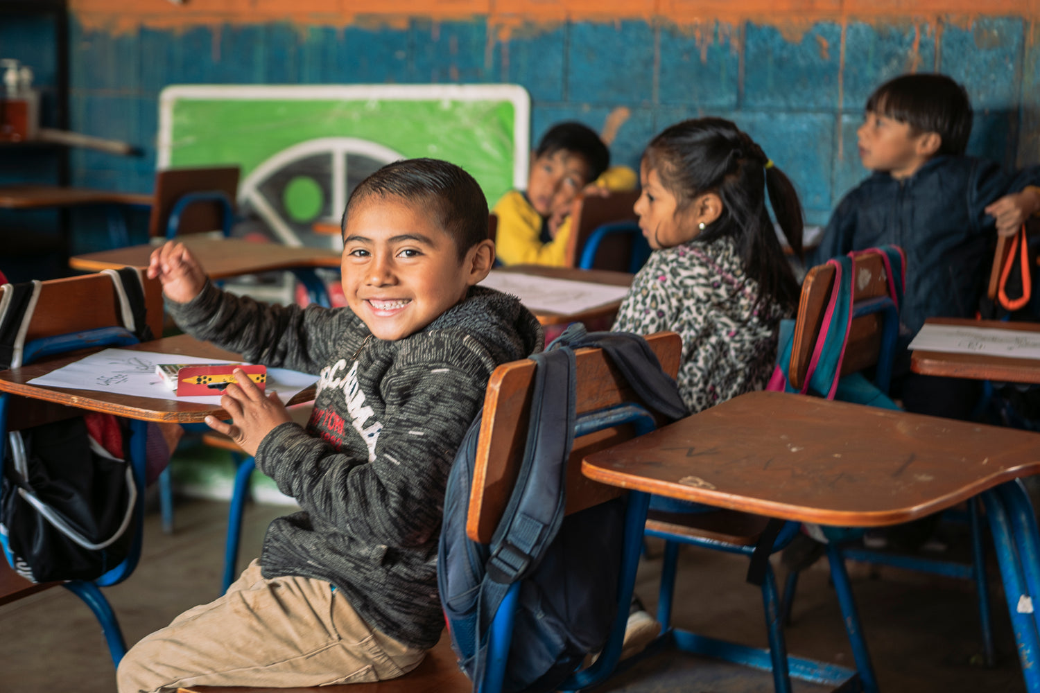 Children sitting at desks in a classroom with a green chalkboard.