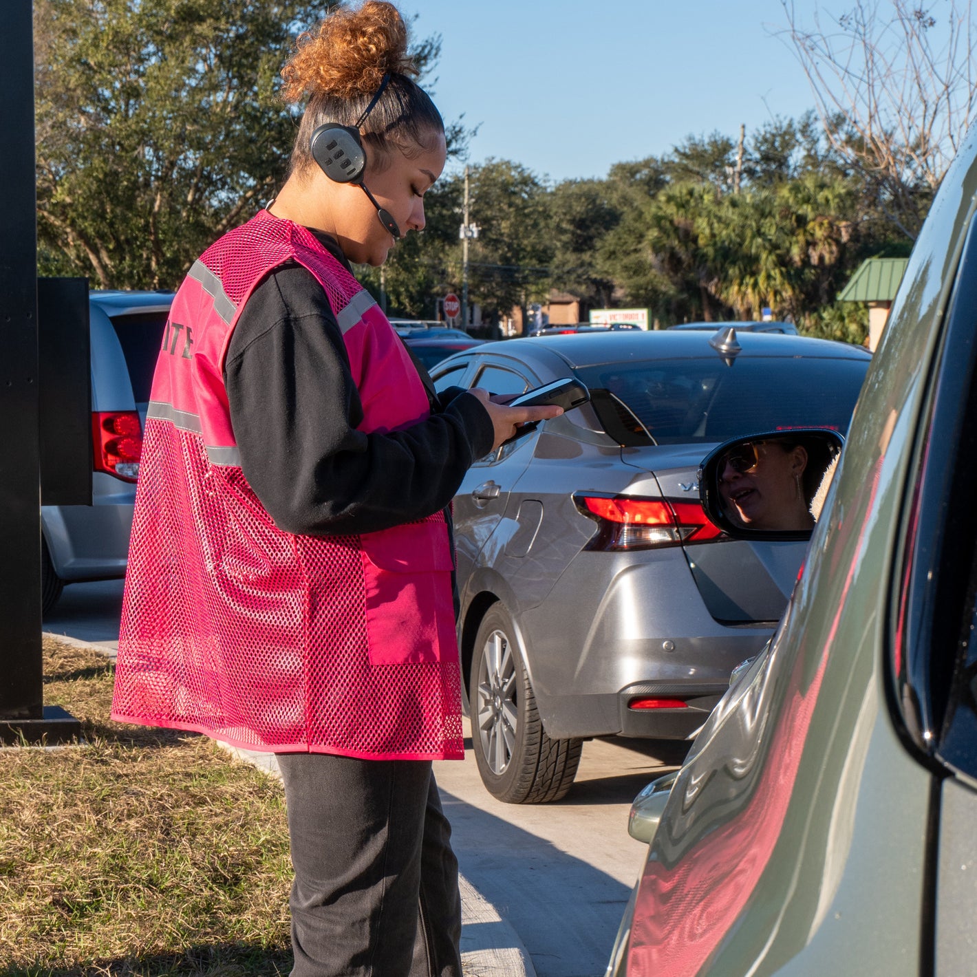 Person in a pink safety vest using a device taking orders thru the drive thru.